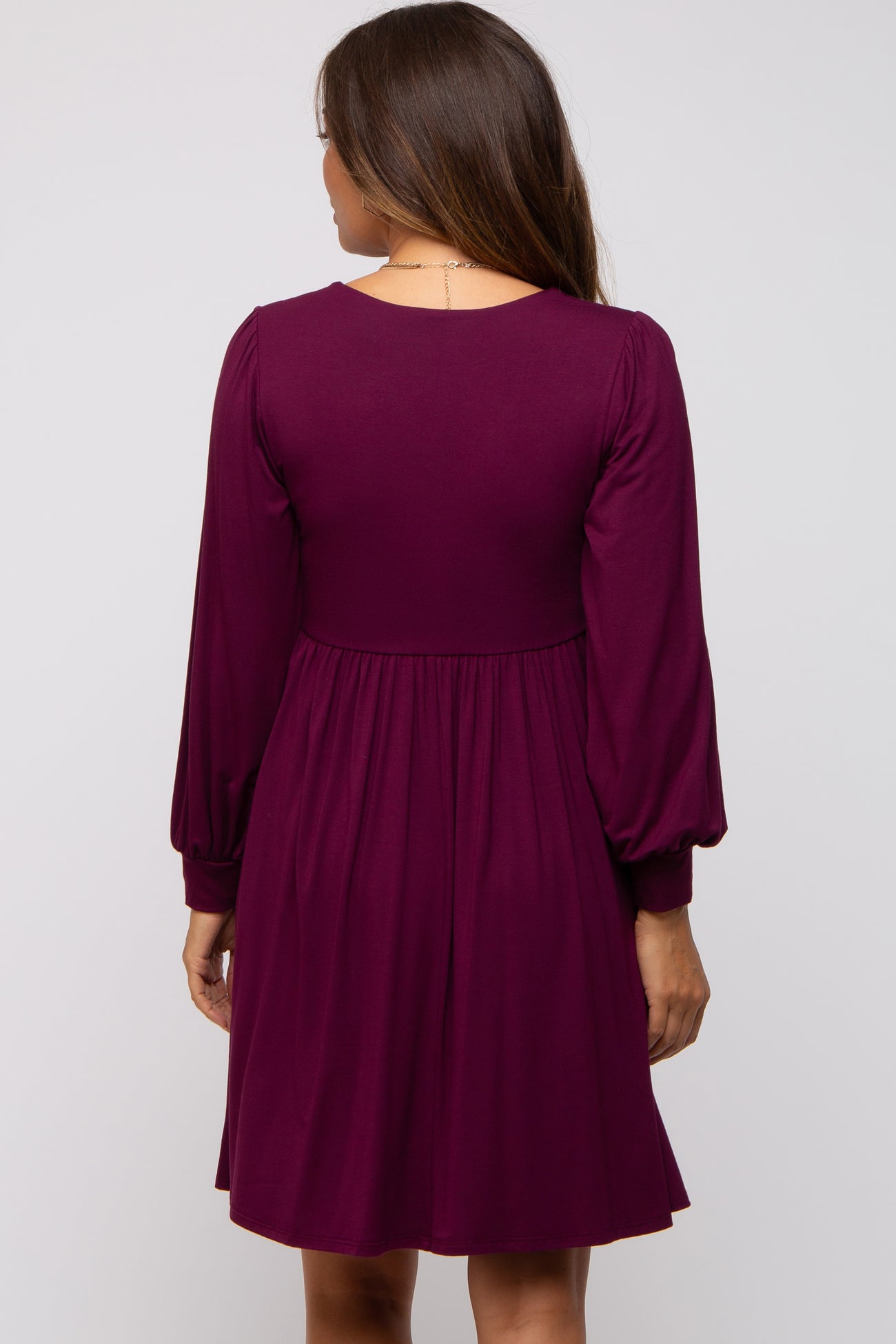 woman wearing a purple long sleeve maternity dress with a fitted bodice and flared skirt, showing the back view