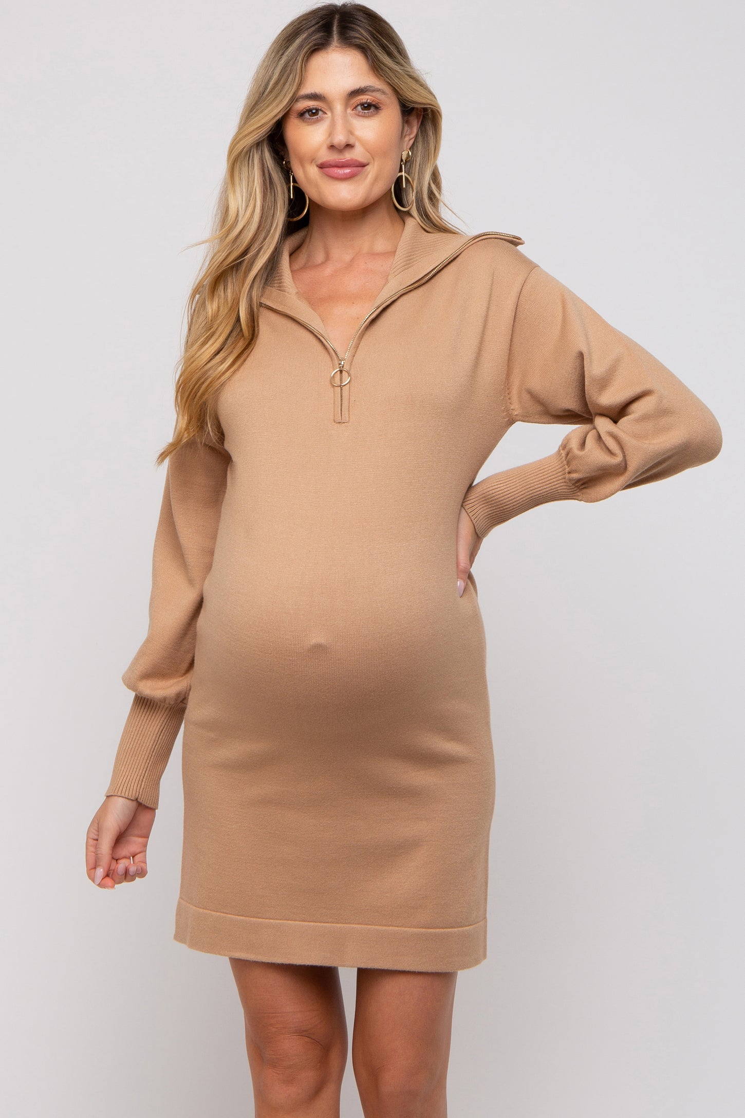 woman wearing a beige long sleeve maternity dress with a quarter zip and a visible baby bump