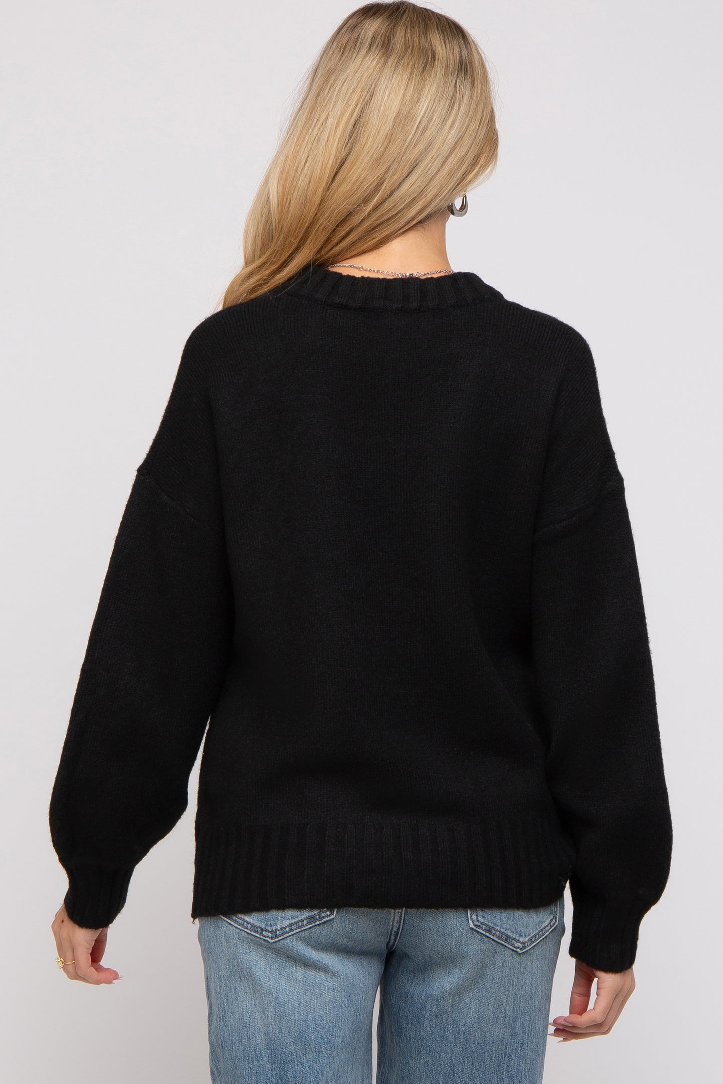 woman wearing a black oversized maternity sweater with a relaxed fit and drop sleeves, seen from the back