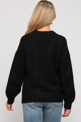 woman wearing a black oversized maternity sweater with a relaxed fit and drop sleeves, seen from the back