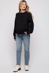 woman wearing a black maternity sweater and light blue jeans, with a visible baby bump