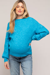 woman wearing a bright blue oversized maternity sweater and showing her baby bump while posing confidently