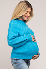 woman wearing a bright blue maternity sweater, gently cradling her baby bump, with light jeans and a relaxed fit