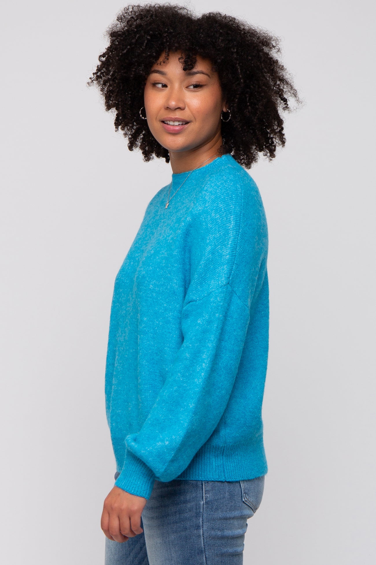 woman wearing a bright turquoise cozy sweater with long sleeves and a relaxed fit, posing sideways