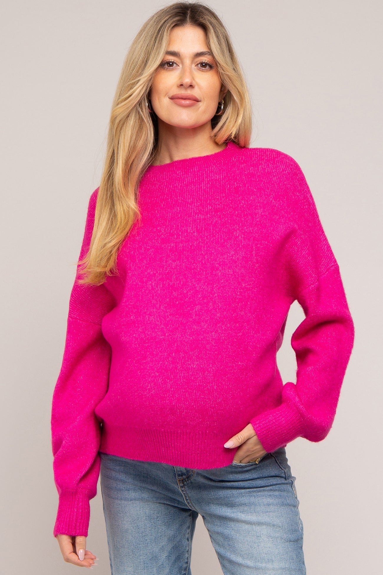 woman wearing a bright pink maternity sweater with a relaxed fit and long sleeves, showing her baby bump