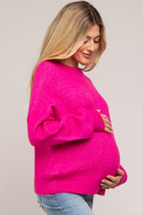 woman wearing a bright pink maternity sweater while holding her baby bump