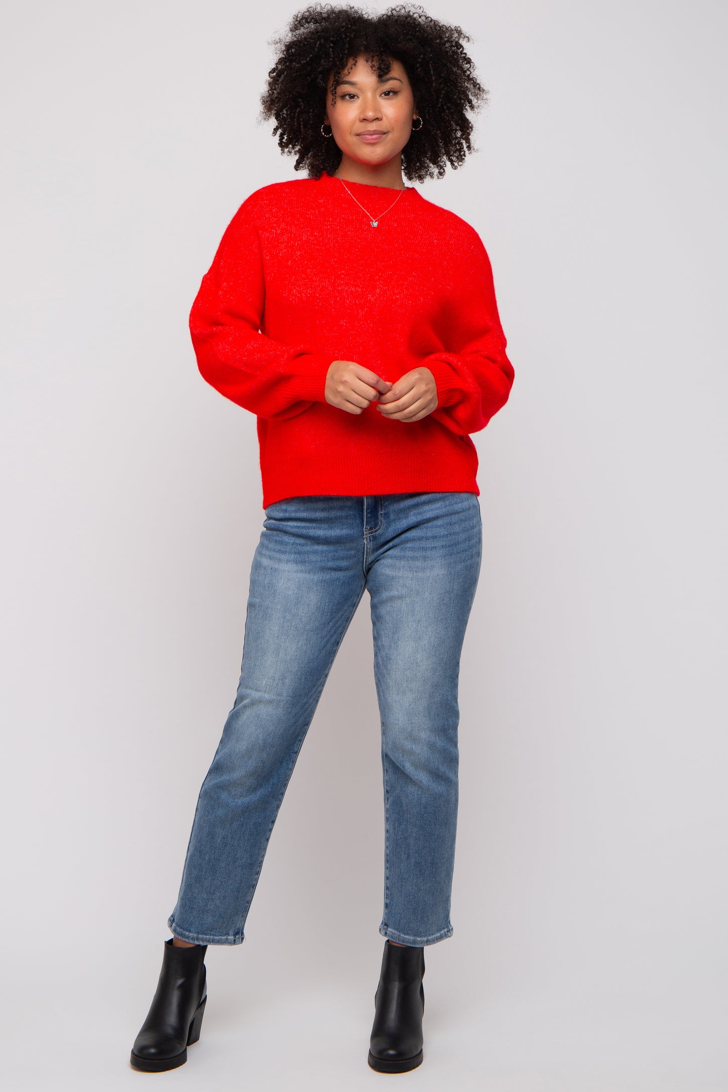 woman wearing a red oversized sweater and light blue straight leg jeans, standing in black ankle boots