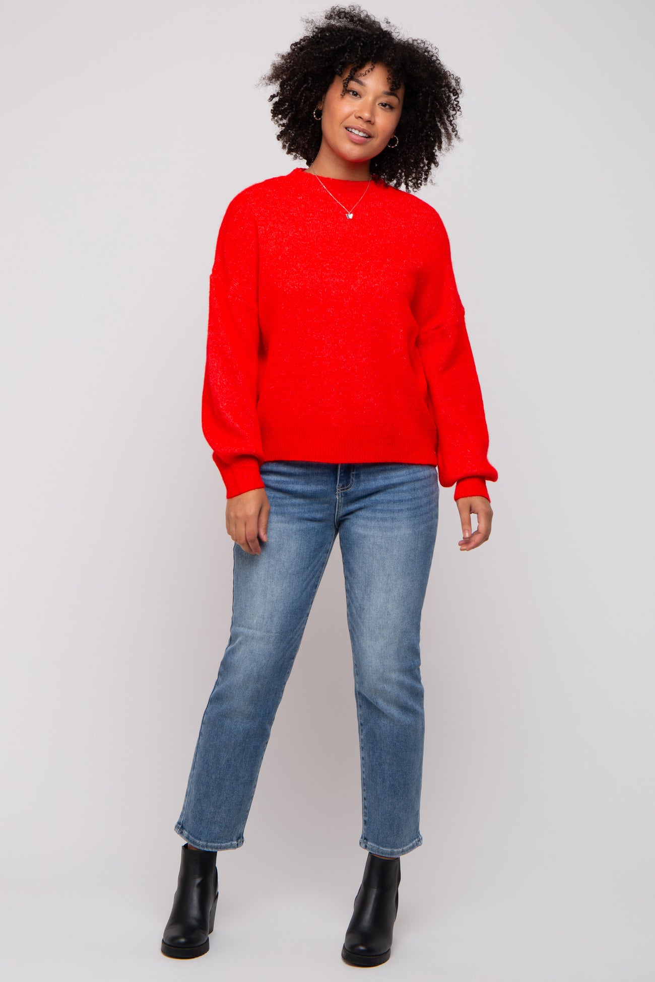 woman wearing a bright red oversized sweater and blue straight leg jeans, paired with black ankle boots