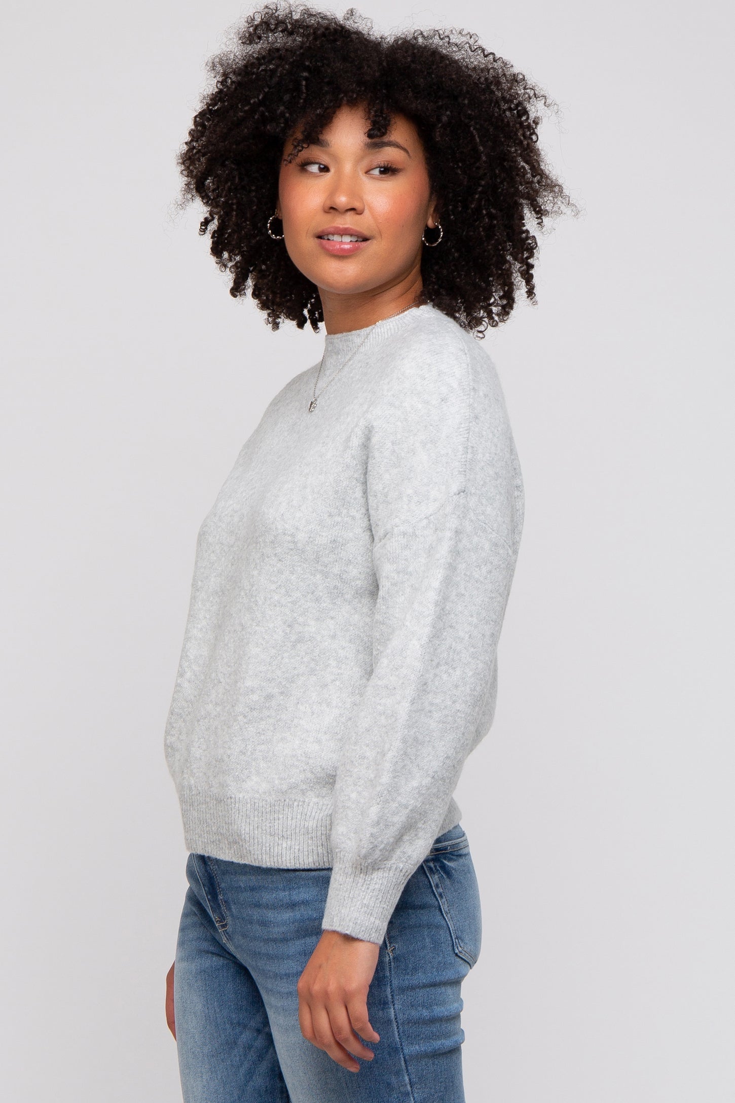 woman wearing a light gray sweater with a round neckline and long sleeves, paired with blue jeans