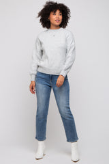 woman wearing a light gray sweater and blue jeans, standing and posing with curly hair and white ankle boots