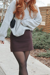 woman wearing a gray oversized sweater and a brown mini skirt paired with black tights