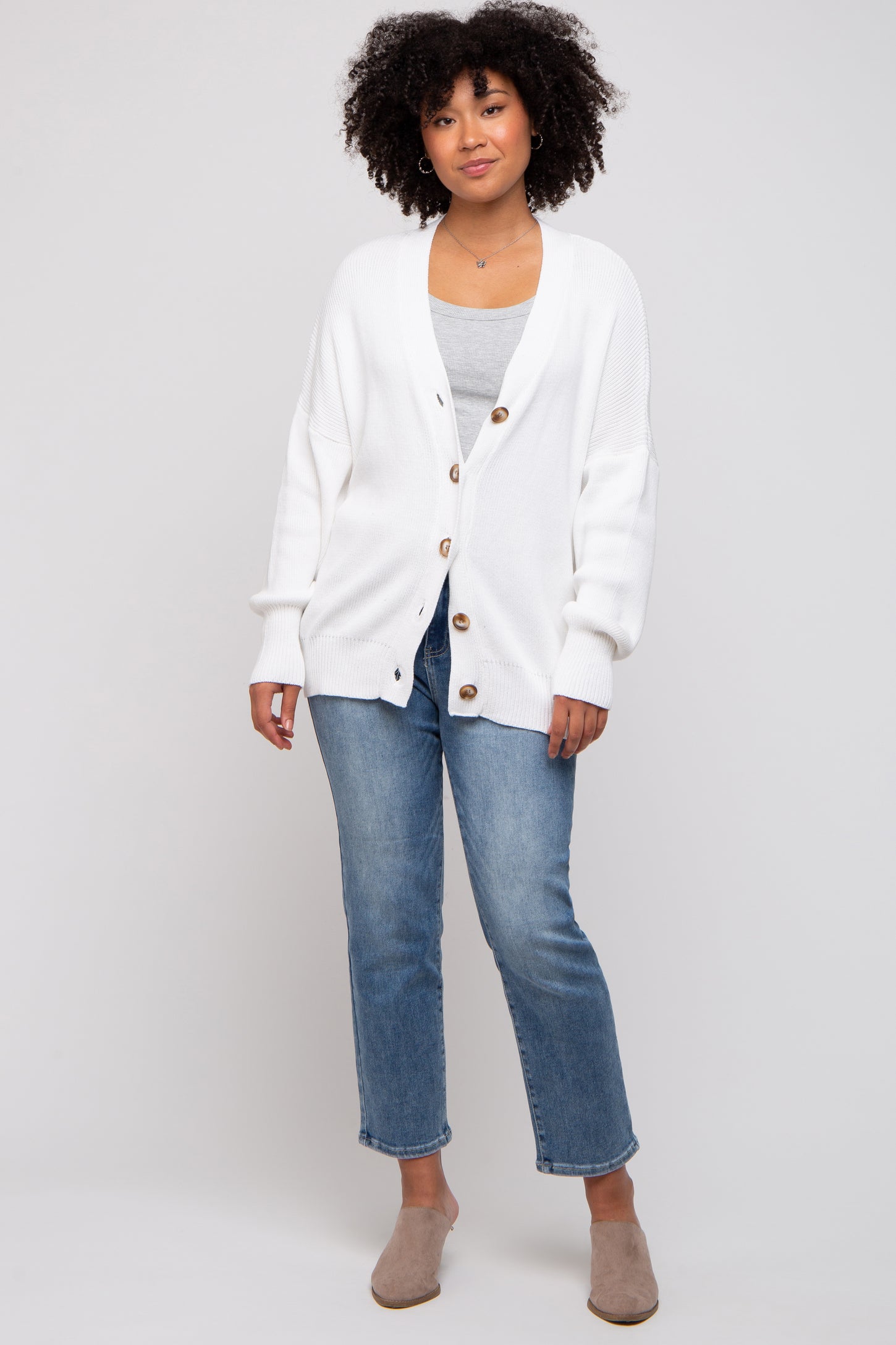 woman wearing a white oversized cardigan with buttons, paired with a gray top and light blue cropped jeans