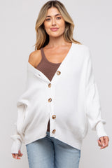 woman wearing a white oversized maternity cardigan with buttons over a brown tank top and light blue jeans