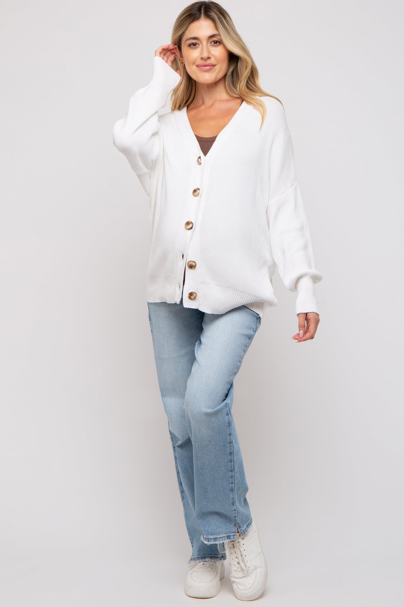 woman wearing a white button-up maternity cardigan over a black top and blue jeans, smiling at the camera