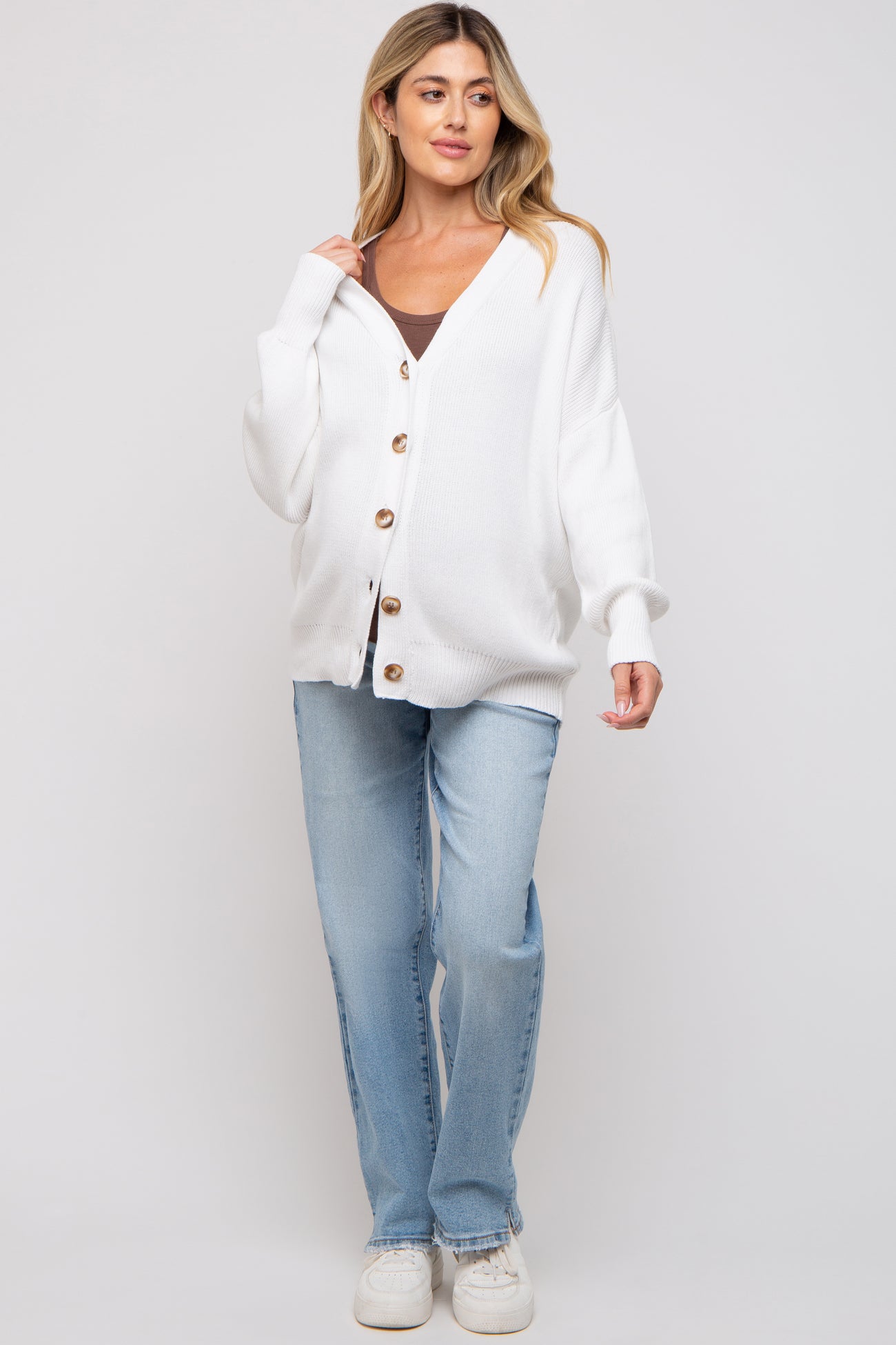woman wearing a white oversized knitted maternity cardigan with buttons, paired with a black tank top and light blue jeans