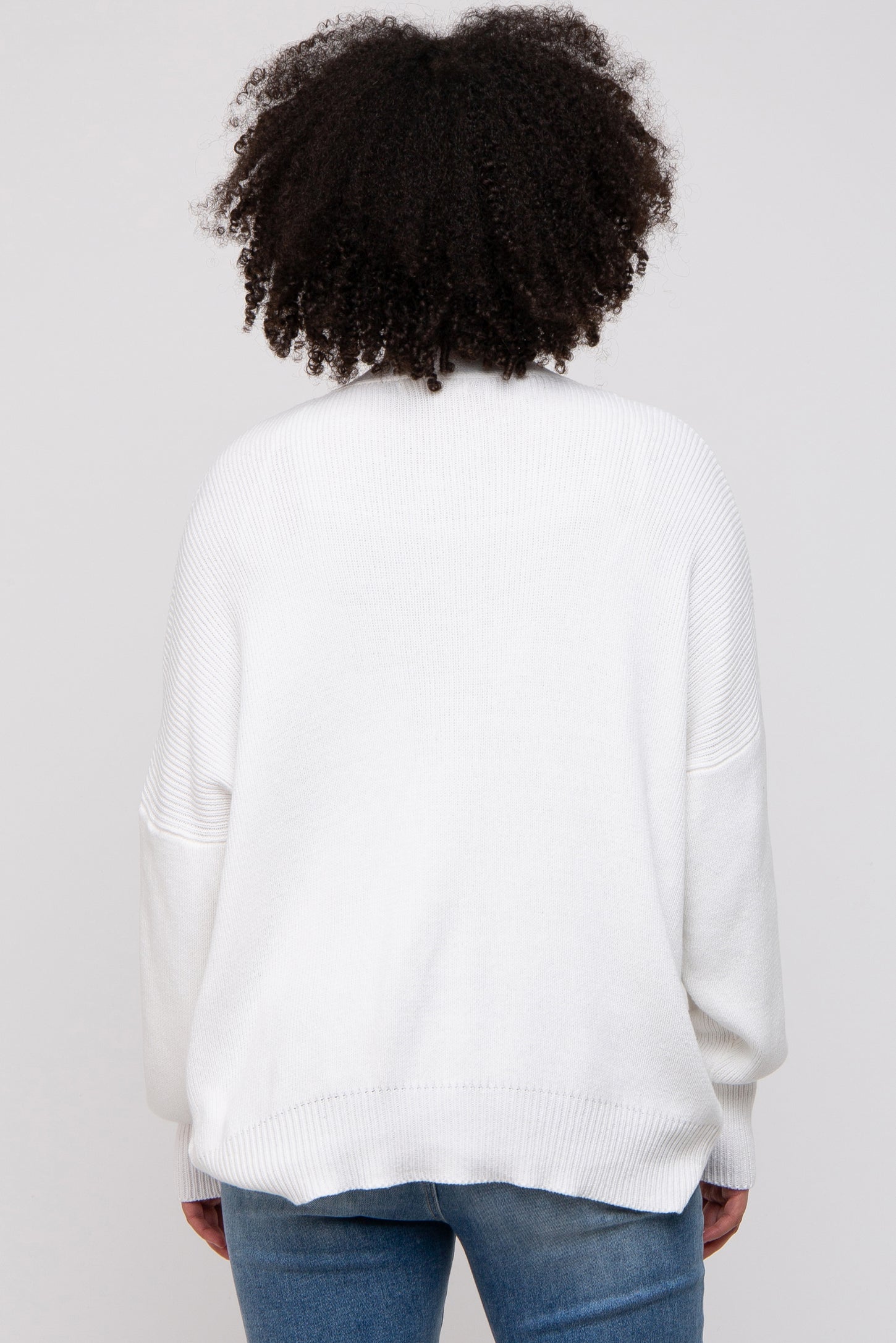 woman wearing a white oversized sweater with ribbed detailing, seen from the back, paired with blue jeans