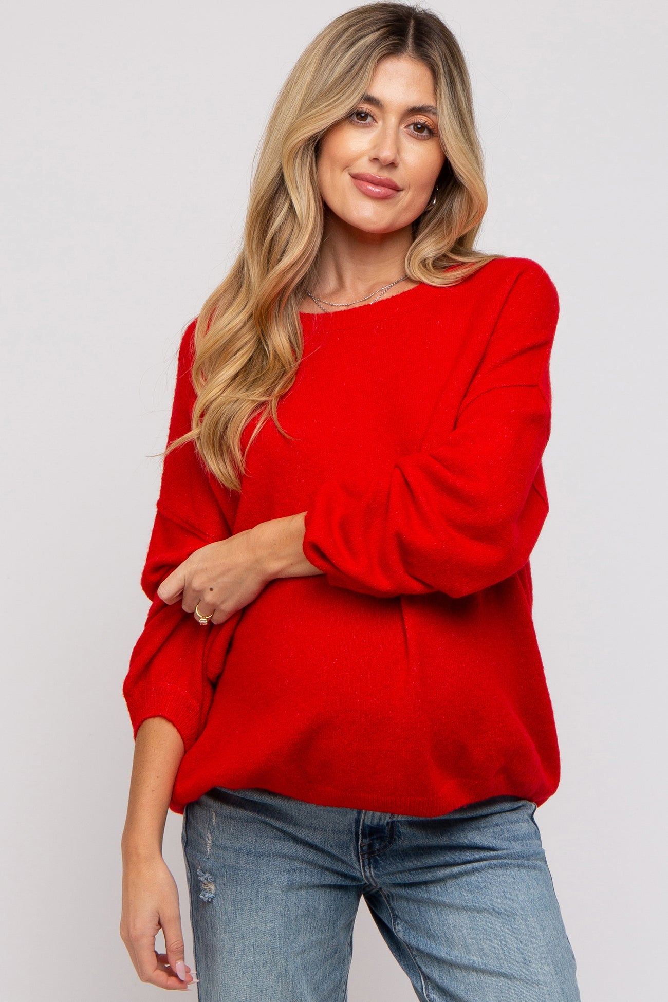 woman wearing a red oversized maternity sweater with balloon sleeves and paired with light blue jeans