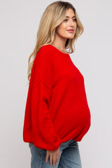 woman wearing a red oversized maternity sweater with a visible baby bump and blue jeans