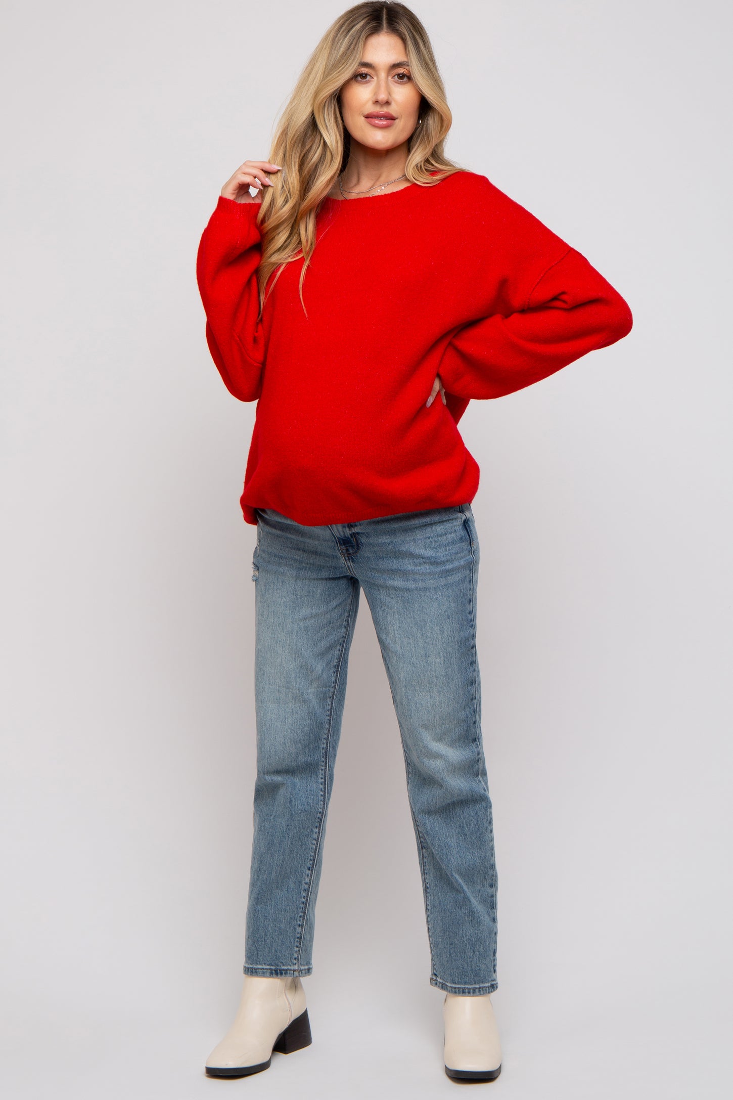 woman wearing a red oversized maternity sweater with a visible baby bump and blue jeans