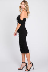 woman wearing a black off-the-shoulder bodycon dress with ruching details and high heels