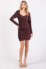 woman wearing a burgundy sparkly bodycon dress with long sleeves and ruching detail