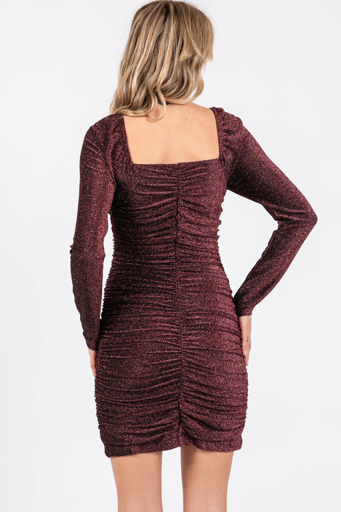 woman wearing a burgundy long sleeve bodycon dress with a square neckline and ruched detailing on the back