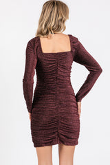 woman wearing a burgundy long sleeve bodycon dress with a square neckline and ruched detailing on the back
