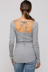 woman wearing a grey long sleeve maternity top with a cut-out back and tie detail, paired with distressed jeans