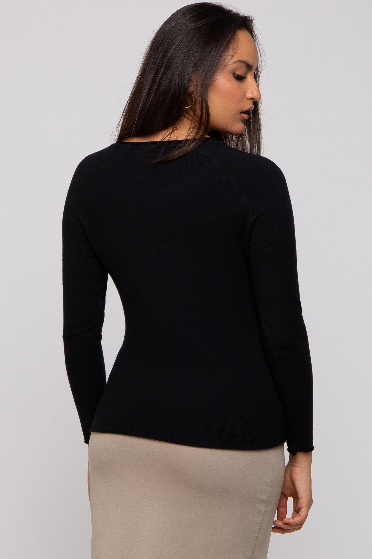 woman wearing a fitted black long sleeve sweater, showing a close back view of the garment
