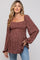 woman wearing a brown floral maternity top with a smocked bodice and puff sleeves, showing her baby bump