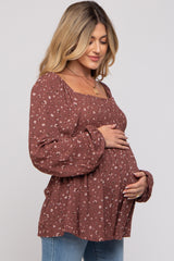 woman wearing a rust floral maternity top with puffed sleeves and holding her baby bump