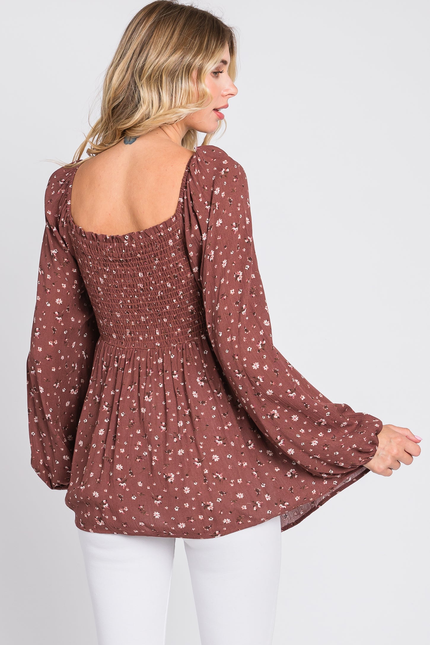 woman wearing a brown floral smocked top with long sleeves and a square neckline, styled with white pants