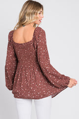 woman wearing a brown floral smocked top with long sleeves and a square neckline, styled with white pants