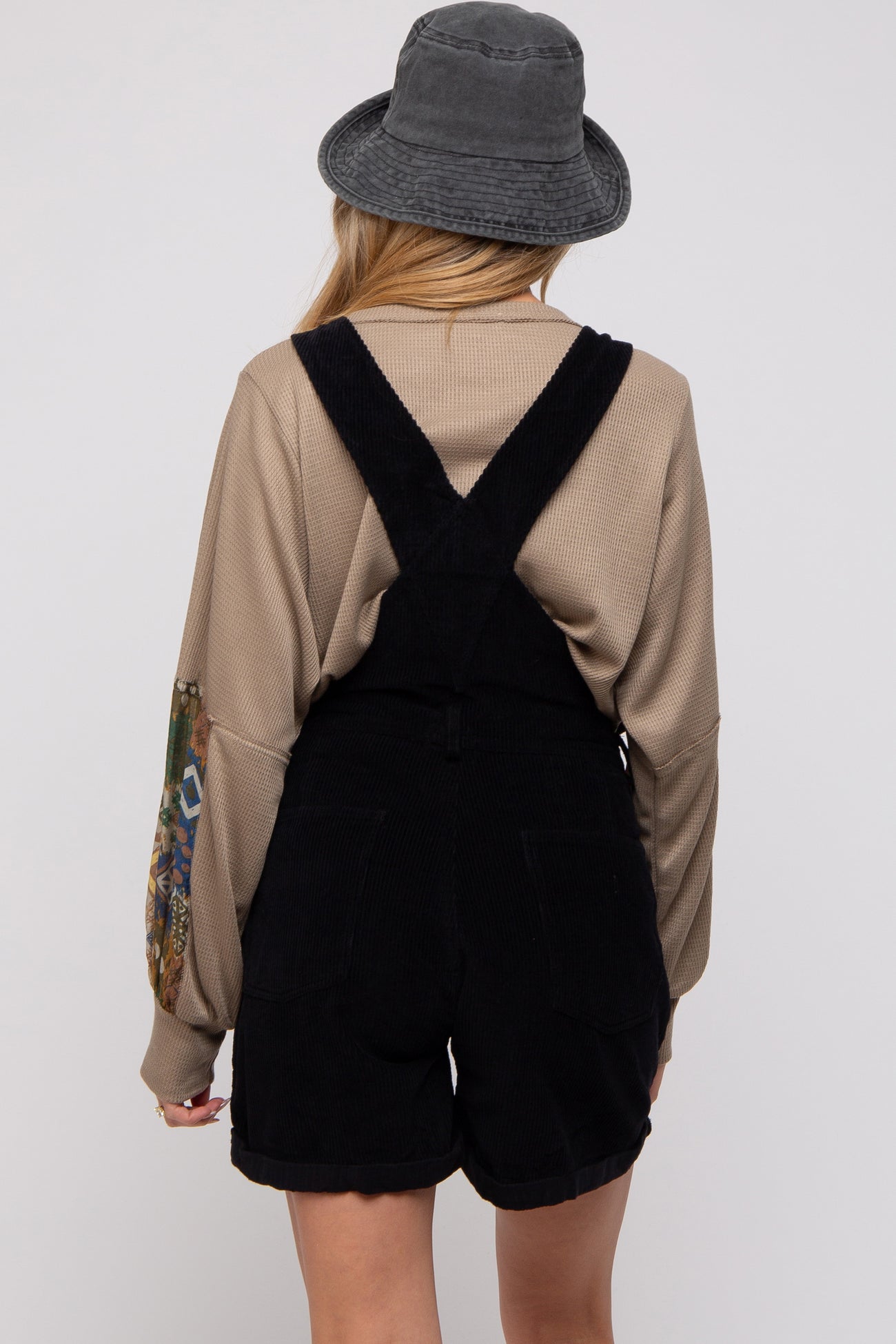 woman wearing a beige long sleeve top with patterned sleeves and black corduroy maternity overalls