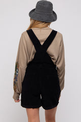 woman wearing a beige long sleeve top with patterned sleeves and black corduroy maternity overalls