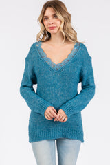 woman wearing a teal oversized sweater with lace trim around the v-neckline and relaxed fit paired with light jeans