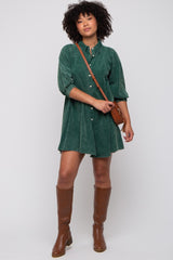 woman wearing a green corduroy button-up dress with three-quarter sleeves and brown knee-high boots