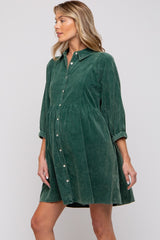 woman wearing a dark green maternity dress with a button-up front and a gathered waist, showcasing her baby bump