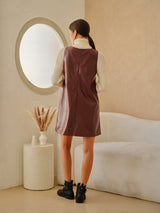woman wearing a burgundy leather sleeveless dress with a white turtleneck sweater, viewed from the back