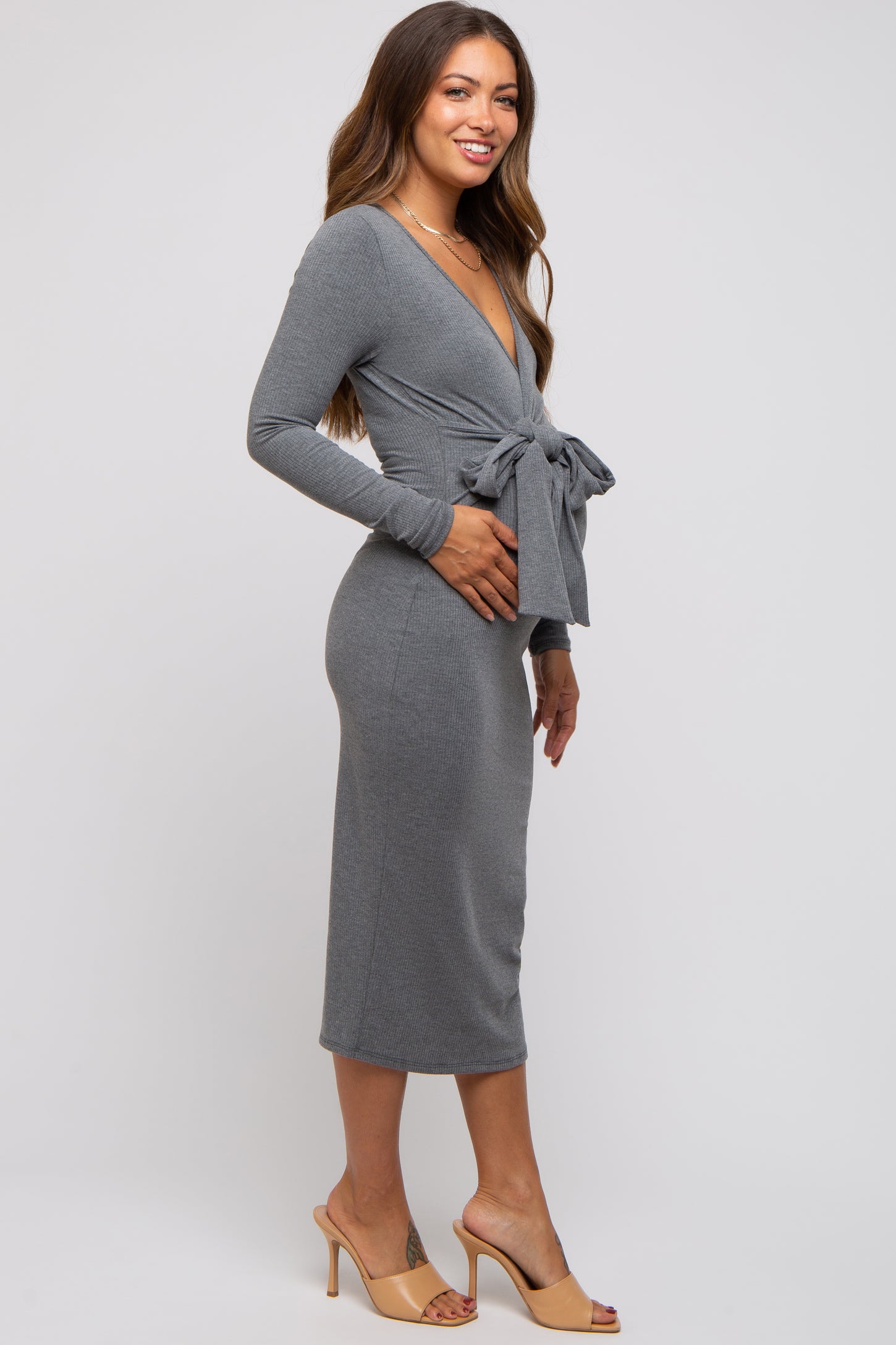 woman wearing a gray long sleeve maternity wrap dress with a tie waist and holding her baby bump