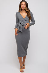woman wearing a grey long sleeve maternity dress with a tie at the waist and holding her baby bump