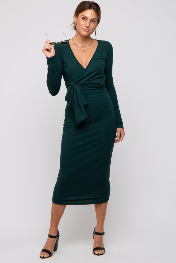 woman wearing a dark green long sleeve wrap dress with a tie detail and holding sunglasses