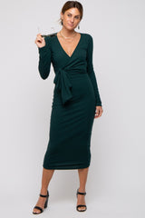 woman wearing a dark green long sleeve wrap dress with a tie detail and holding sunglasses