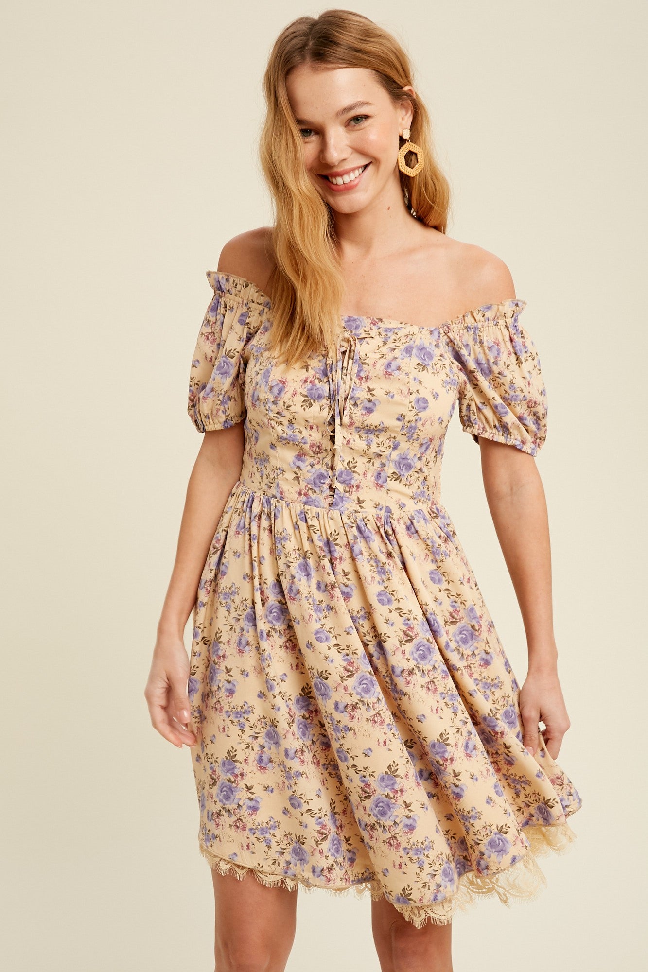 woman wearing a yellow off-shoulder floral dress with puff sleeves and a lace hem, smiling at the camera