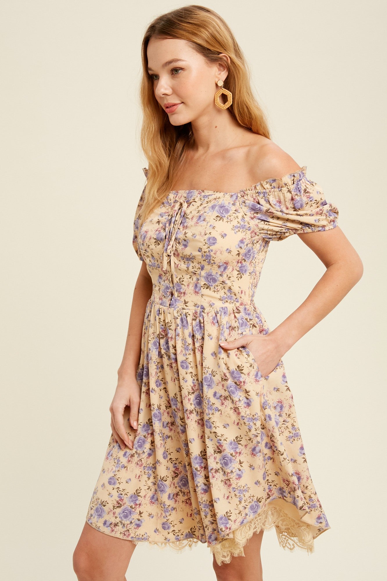 woman wearing a yellow floral off-the-shoulder dress with puffed sleeves and pockets, styled with round earrings