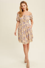 woman wearing a yellow floral off-shoulder dress with puff sleeves and lace trim, standing with one hand in a pocket