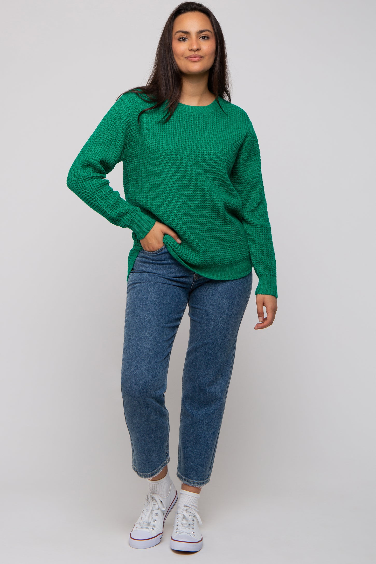 woman wearing a bright green knit sweater paired with blue jeans and white sneakers