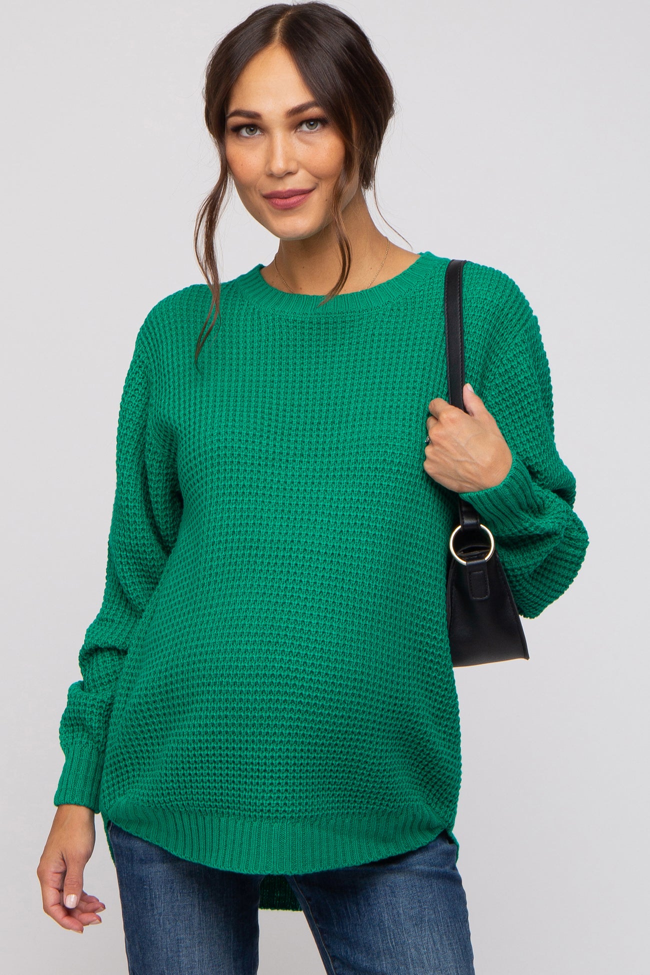 woman wearing a green oversized knit maternity sweater and holding a black handbag, baby bump visible