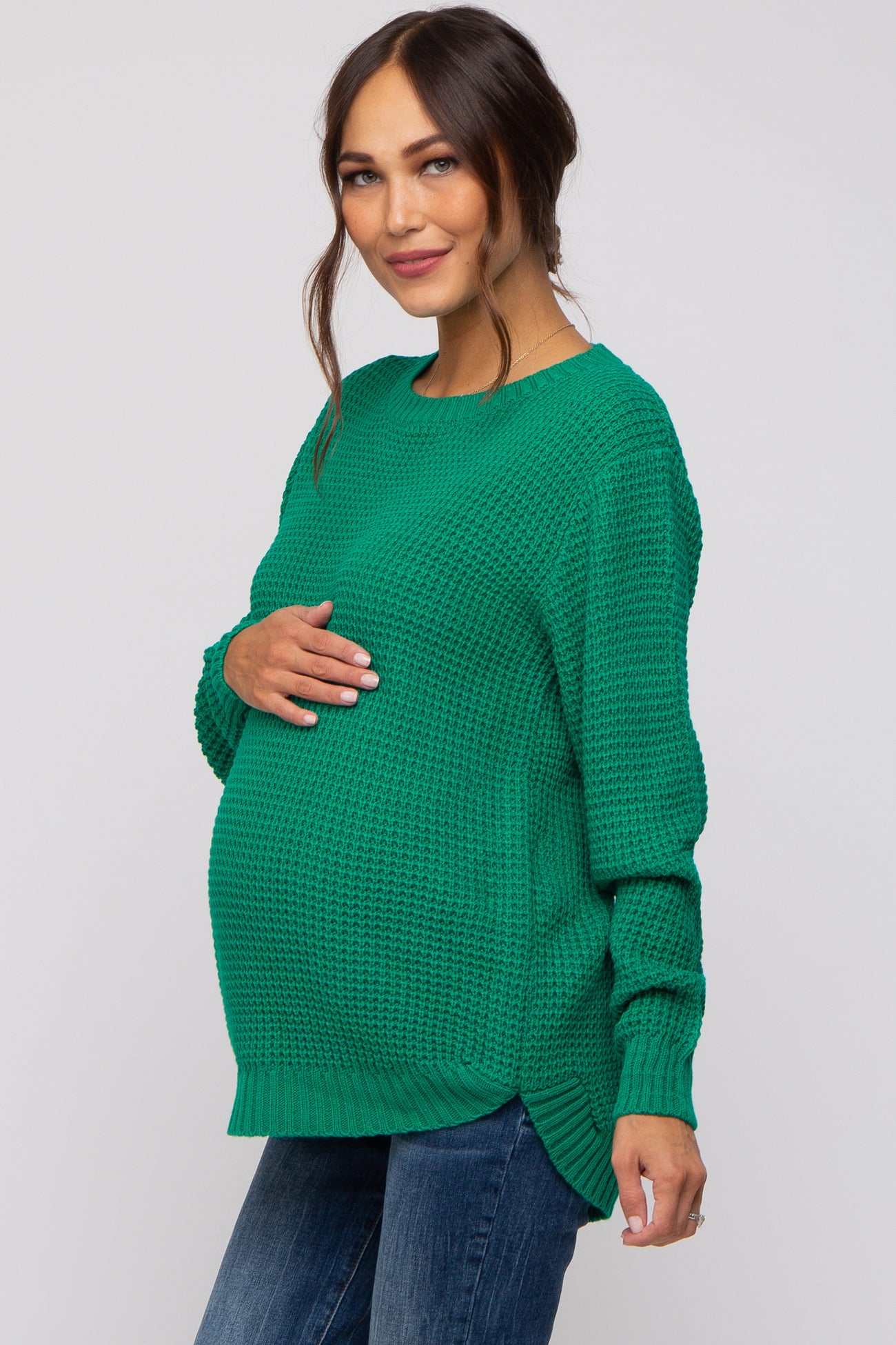 woman wearing a green knit maternity sweater, showing her baby bump, paired with blue jeans