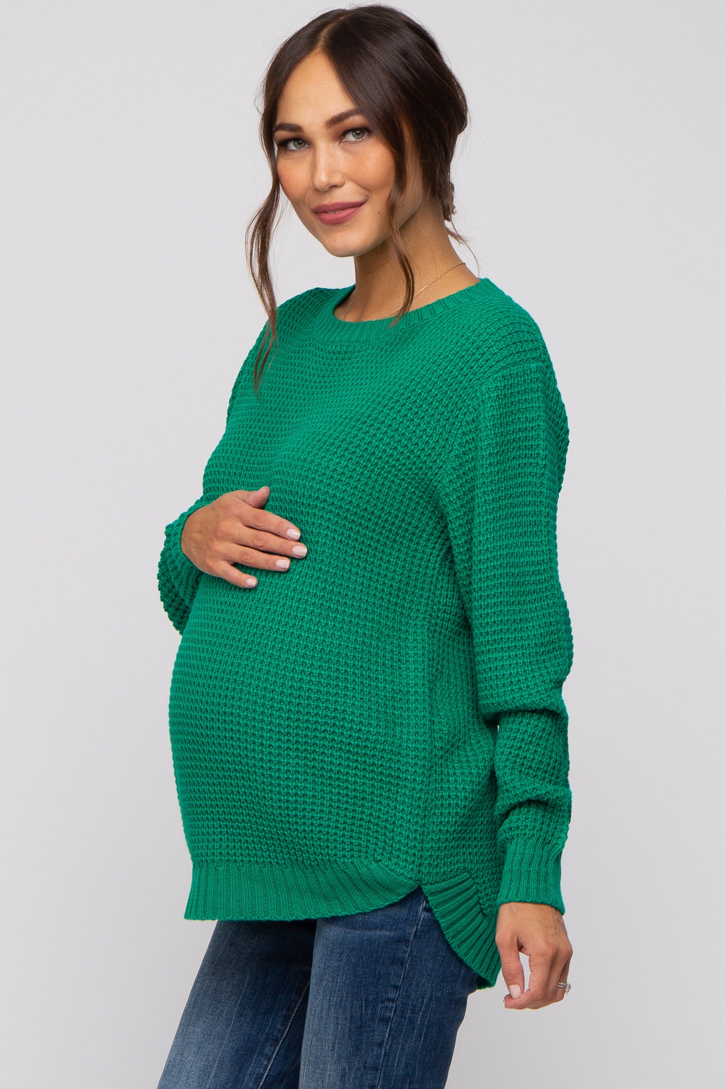 woman wearing a green knit maternity sweater, showing her baby bump, paired with blue jeans